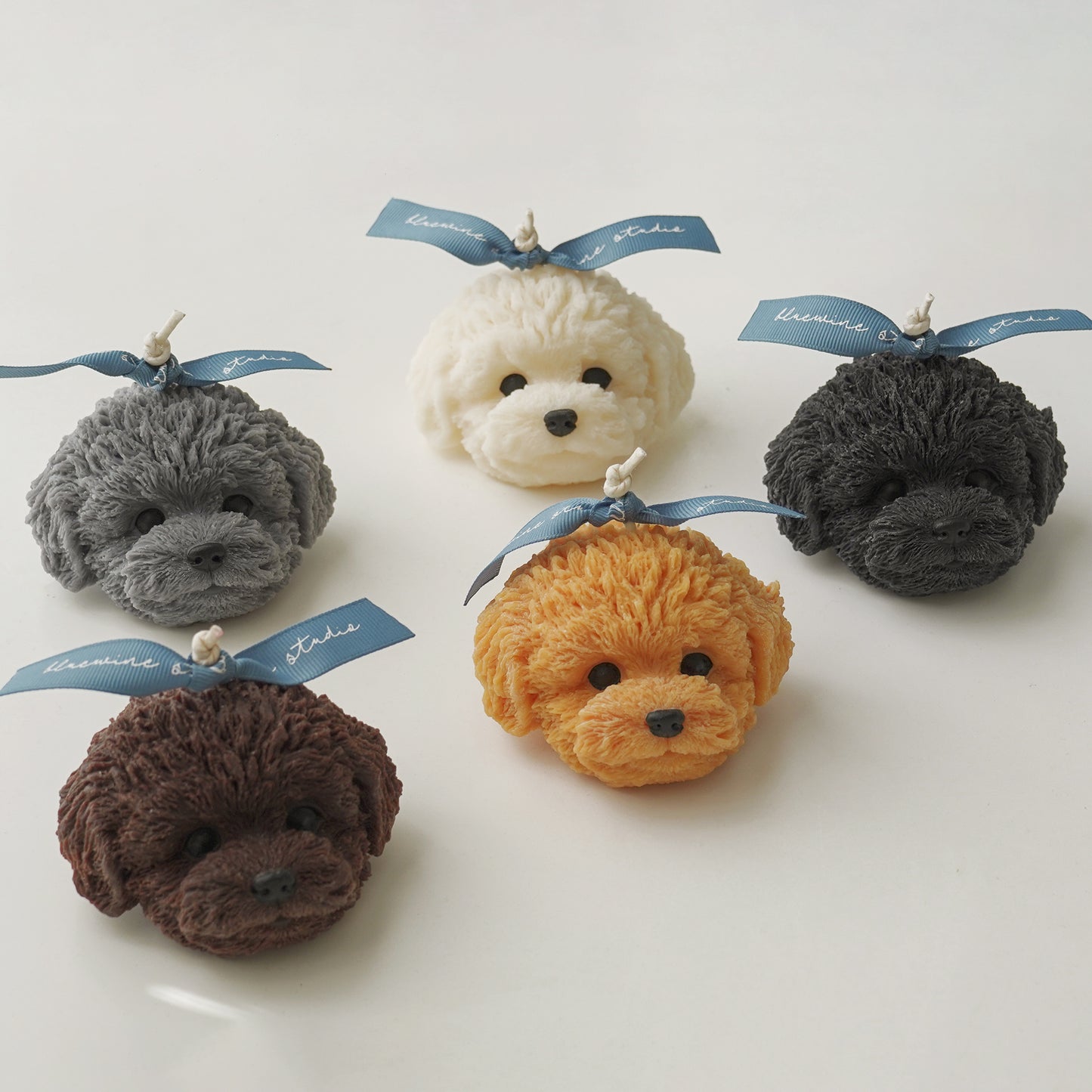 gray poodle, white bichon, chocolate poodle, goldendoodle, black poodle candle placed on a white table