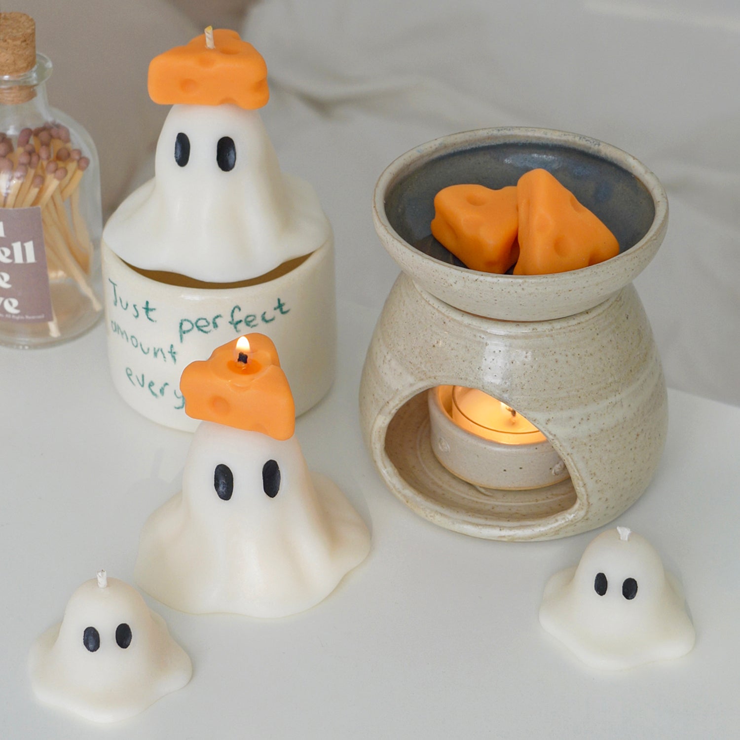 ghost candles with cheese on top, cheese wax melts, wax warmer, mug, and match bottle on a vanity table