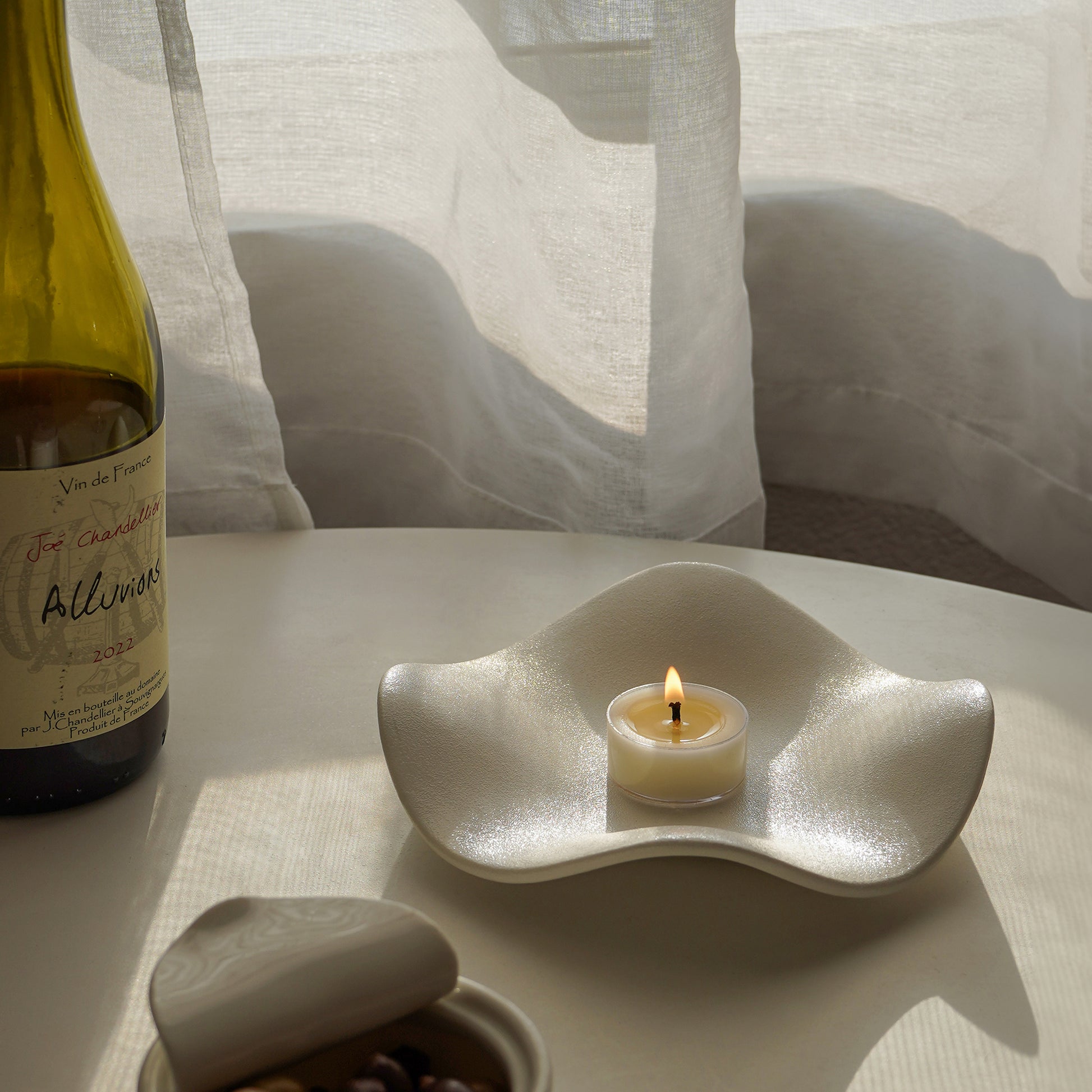 a bottle of red wine and a lit tealight candle placed on a lotus shaped trinket dish on the table