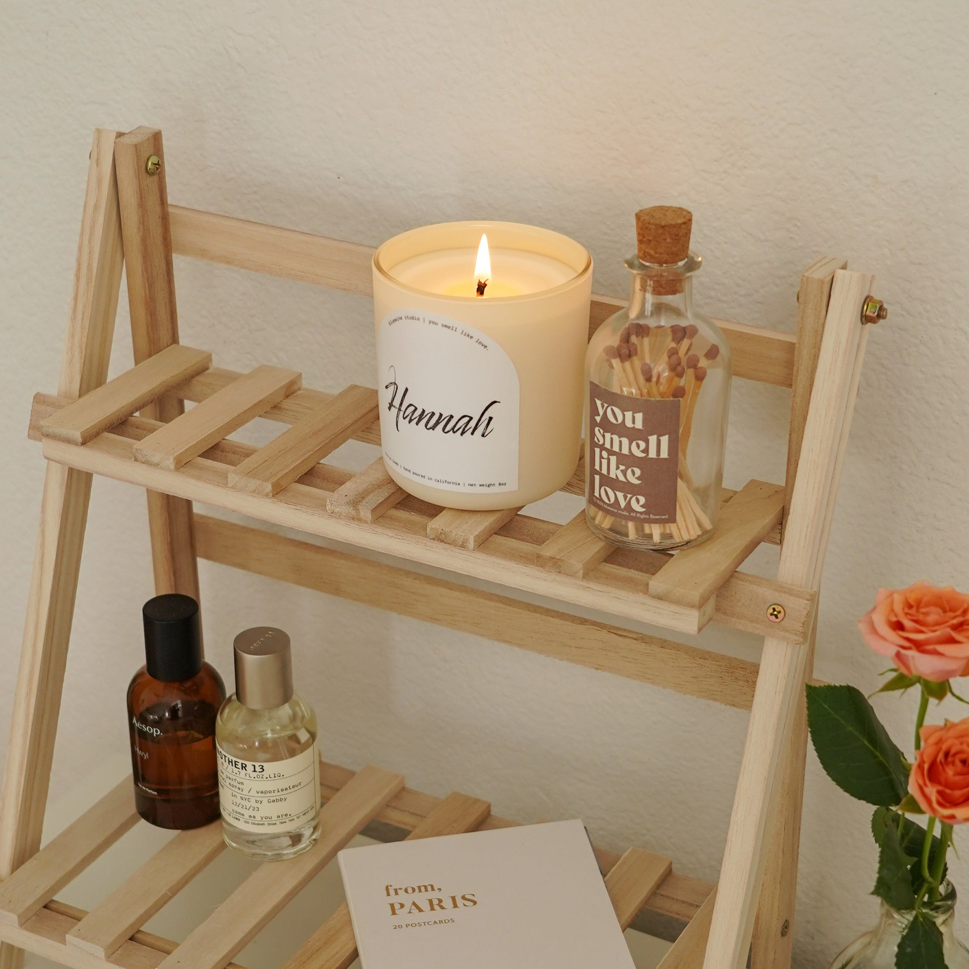 a lit personalized name candle and a match bottle with a brown label placed on a wooden organizer