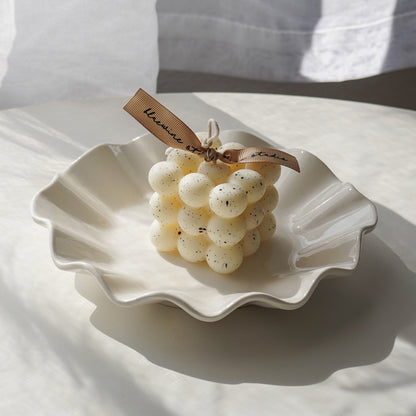 white bubble-shaped cube candle with a black splatter pattern is placed on a white ruffle plate